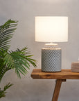 Blue and white ceramic table lamp with white shade on wooden console lit 